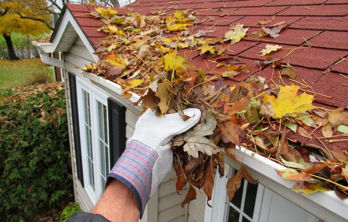 Someone cleaning leaves from their gutters