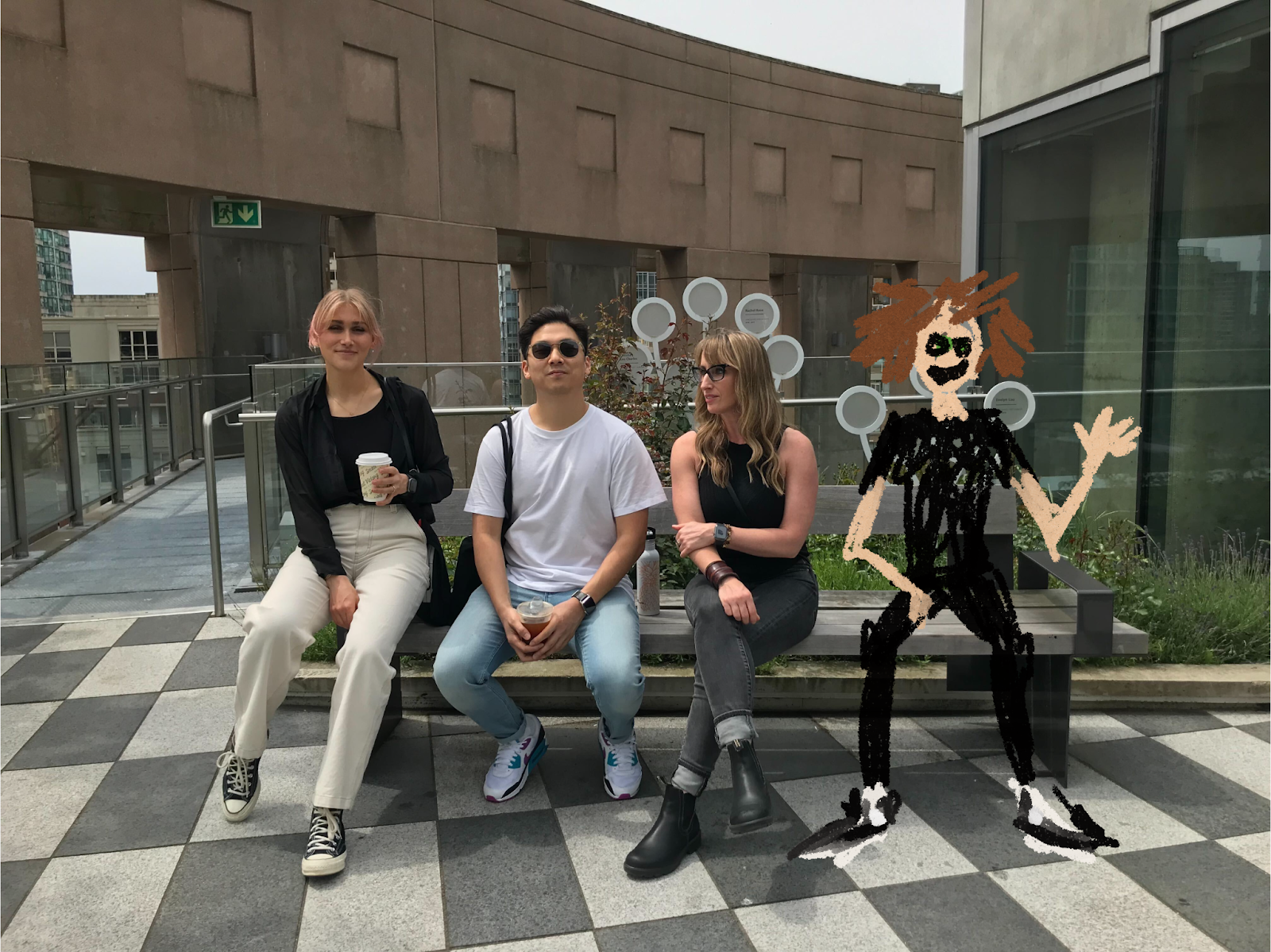 Photo from left to right, Caitlin, James, Lisa, and a hand-drawing of Wil, seated on a bench at Vancouver Library rooftop