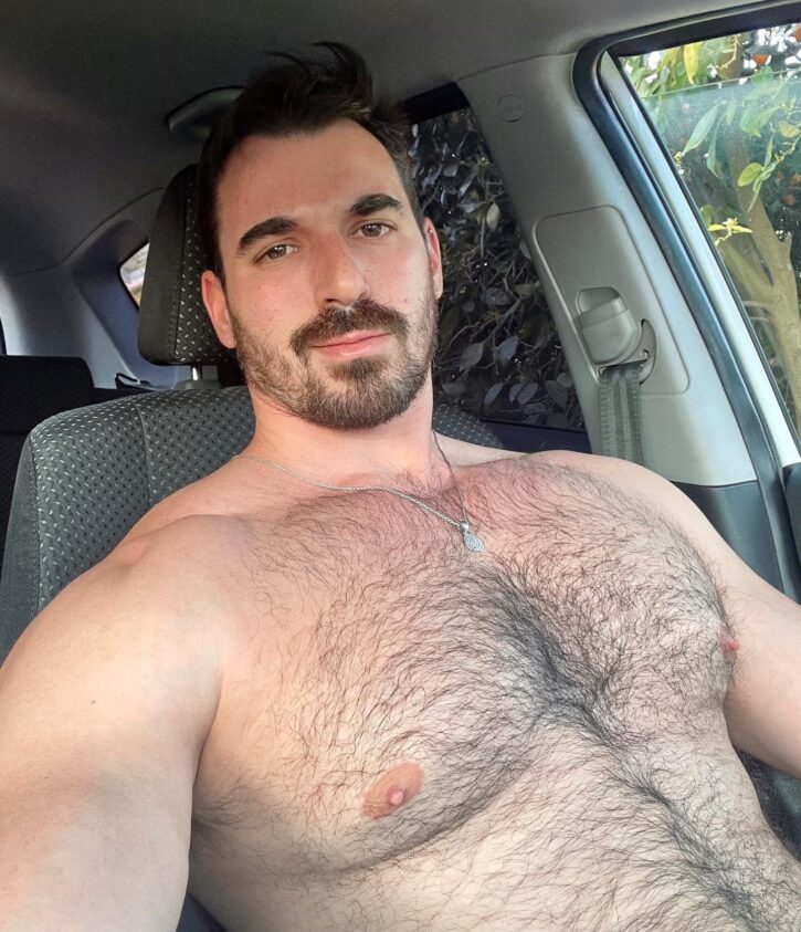 Thick Macho shirtless and smiling while taking a selfie in the car