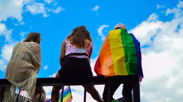 three people in milwaukee rainbow flag sky