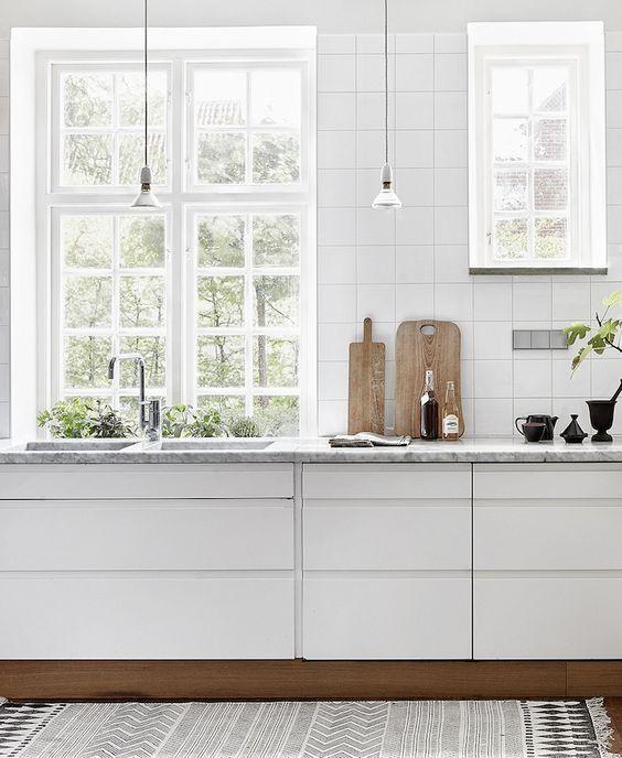 Cozinha com armários brancos, azulejo quadrados brancos, luminárias pendentes e tapete passadeira preto e branco