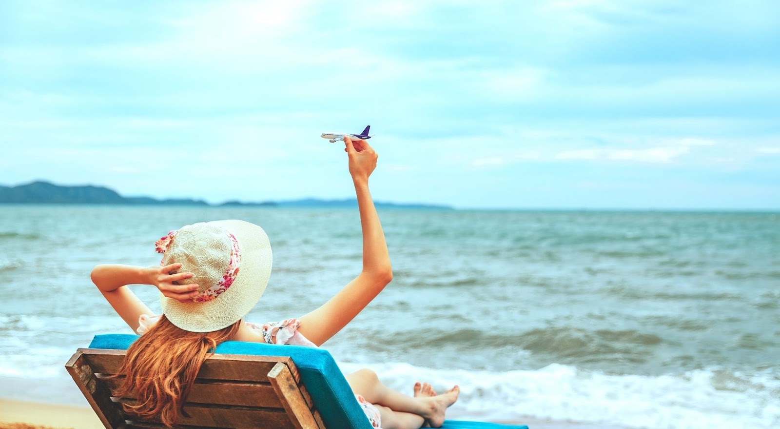 View of woman lounging on a sea bench with a toy plane in her hand.
