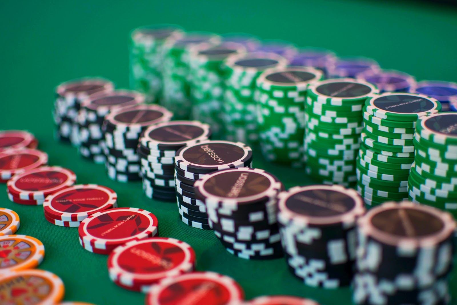 Rows of orange, red, black, green, and blue gambling chips sit on a green betting table 