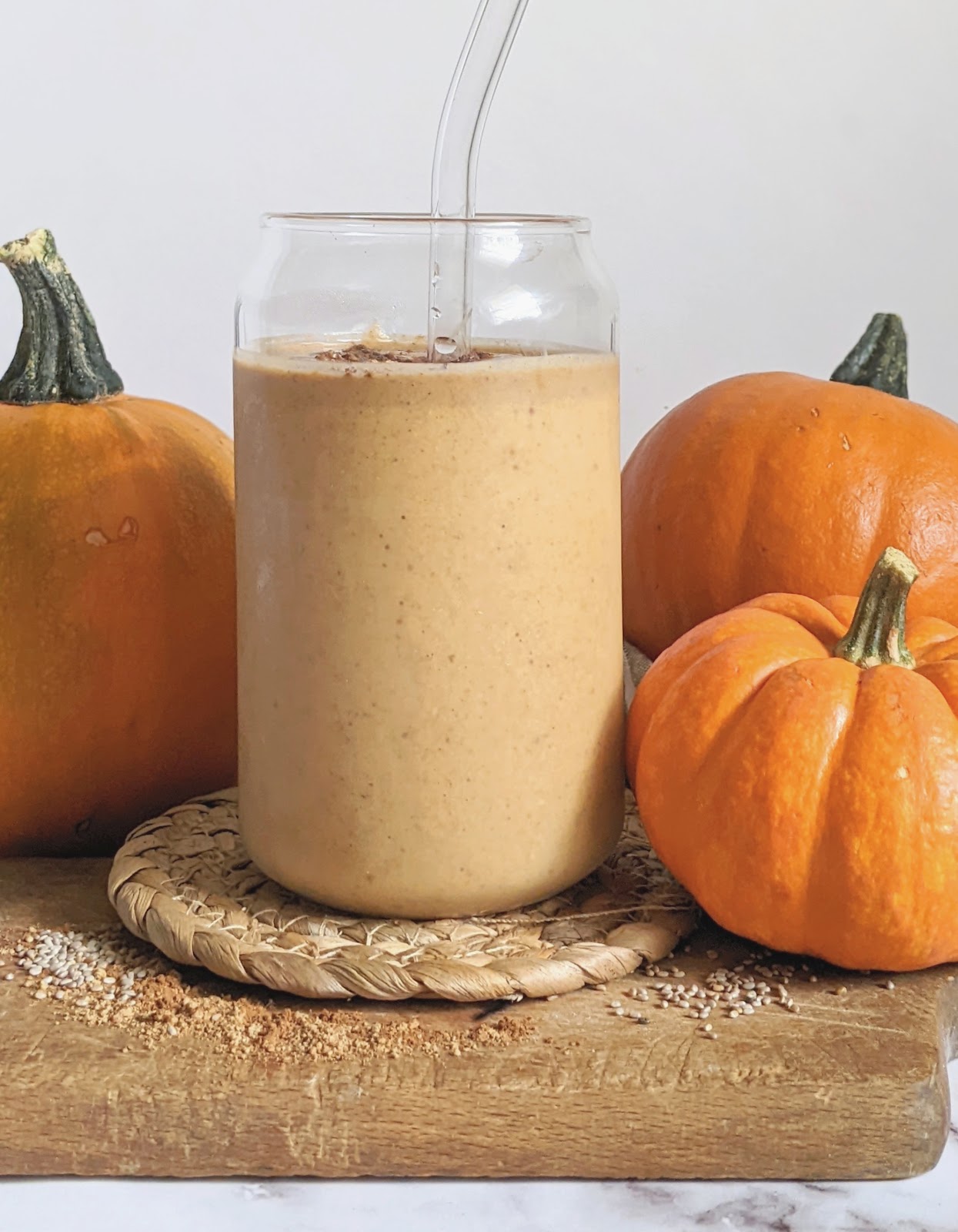 side view of a pumpkin pie smoothie in a glass jar surrounded by pumpkins