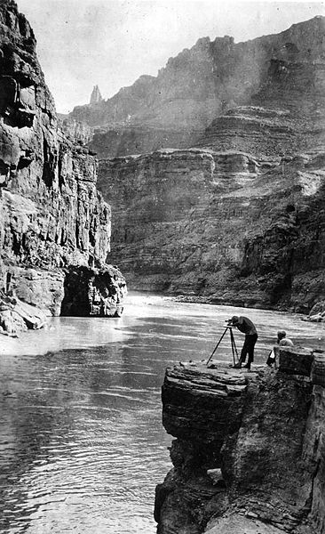 Man standing on a rock of Colorado River with camera stand.