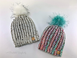 two crochet hats with pom poms lying flat on white background