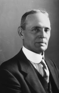 Black and white portrait of Robert Aitken; white man with square hairline wearing a suit staring into the camera