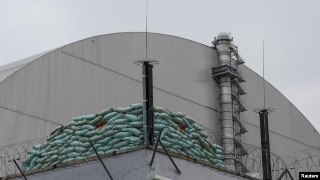 ФАЙЛ — Баррикада из мешков с песком стоит на здании рядом со структурой Нового безопасного конфайнмента (НБК) над старым саркофагом, закрывающим поврежденный четвертый реактор Чернобыльской АЭС, в Чернобыле, Украина, 16 апреля 2022 года.