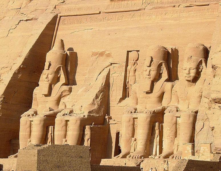 The entrance to Abu Simbel, with three huge statues of gods and one partially destroyed statue. The stone is tan, and the surviving statues have impressive hats on.