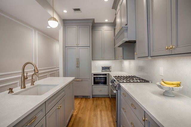 grey galley kitchen with grey shaker cabinets, brass hardware, wood floors and grey paneled appliances