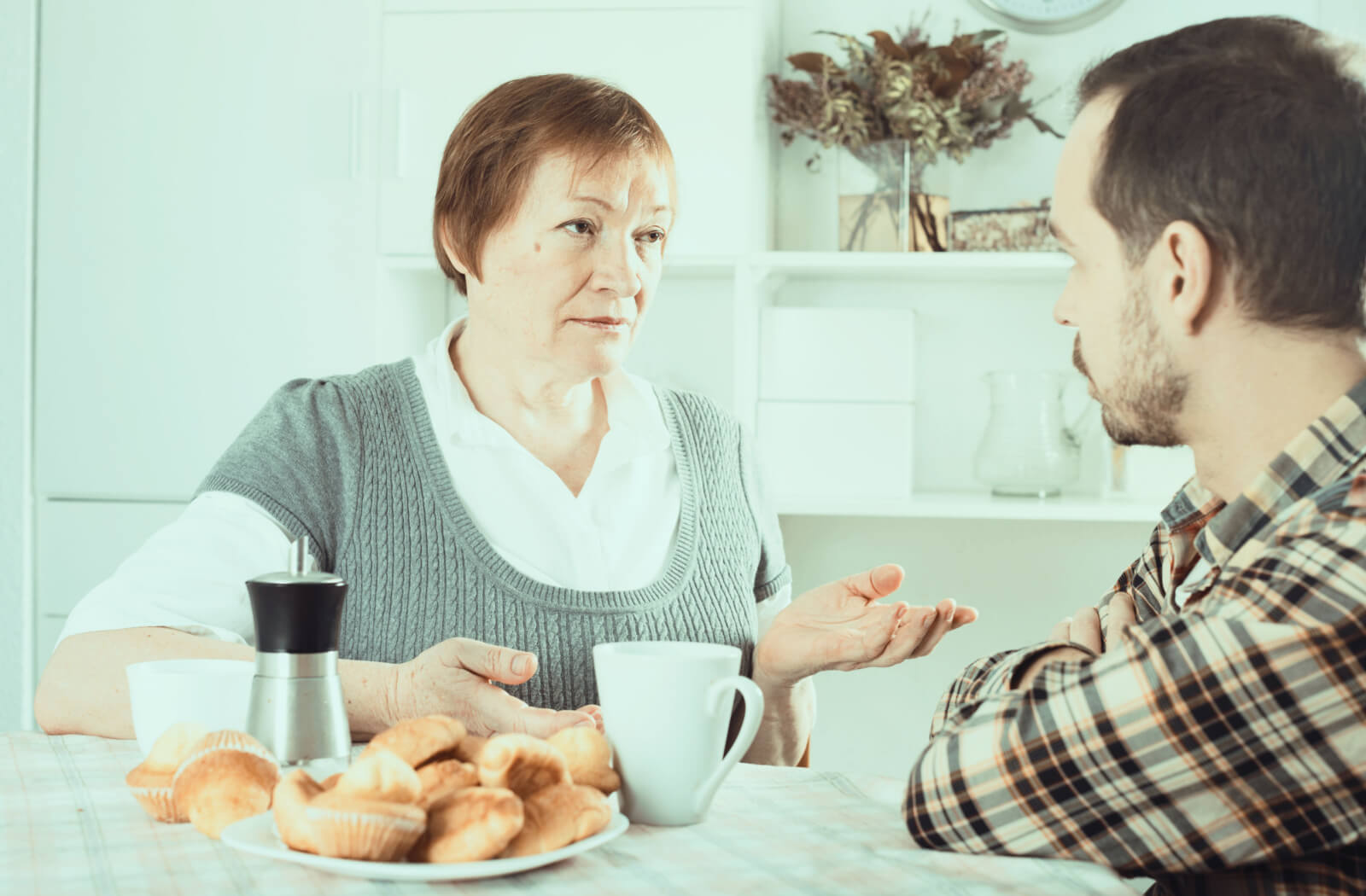 A senior woman talking seriously to his son while having a cup of tea and bread.