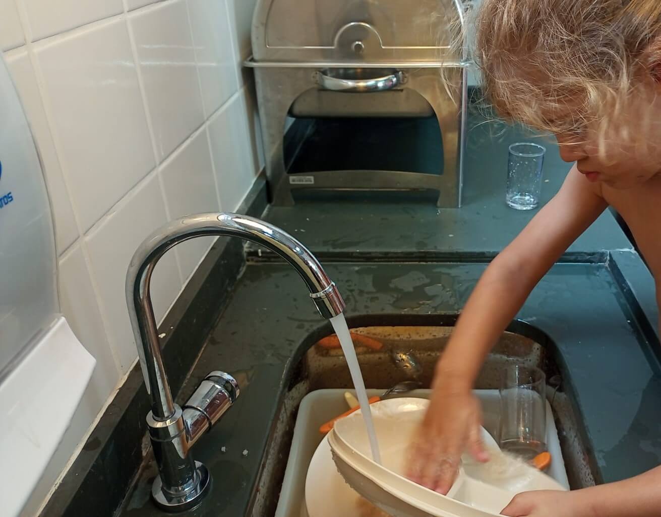 A imagem mostra uma criança lavando louça.