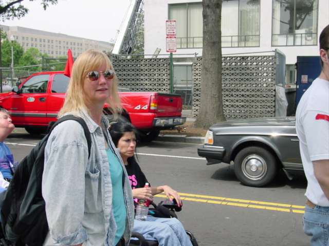 Blonde woman in sunglasses smiles at the camera while dark-haired woman using a wheelchair looks stern. 