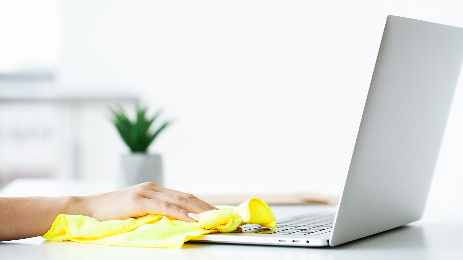 Hand wiping down laptop and desk with a yellow cloth