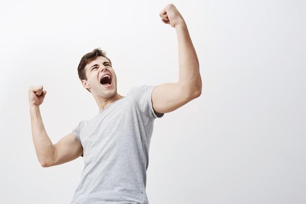 Close up of successful young caucasian male sportsman screaming yes and raising clenched fists in the air, feeling excited. people, success, triumph, victory, winning and celebration.