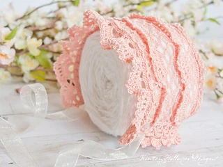 lacy pink baby bonnet on yarn cake with flowers in background