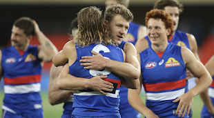 Photo of AFL athletes hugging on the field, featuring Bailey Smith's mullet
