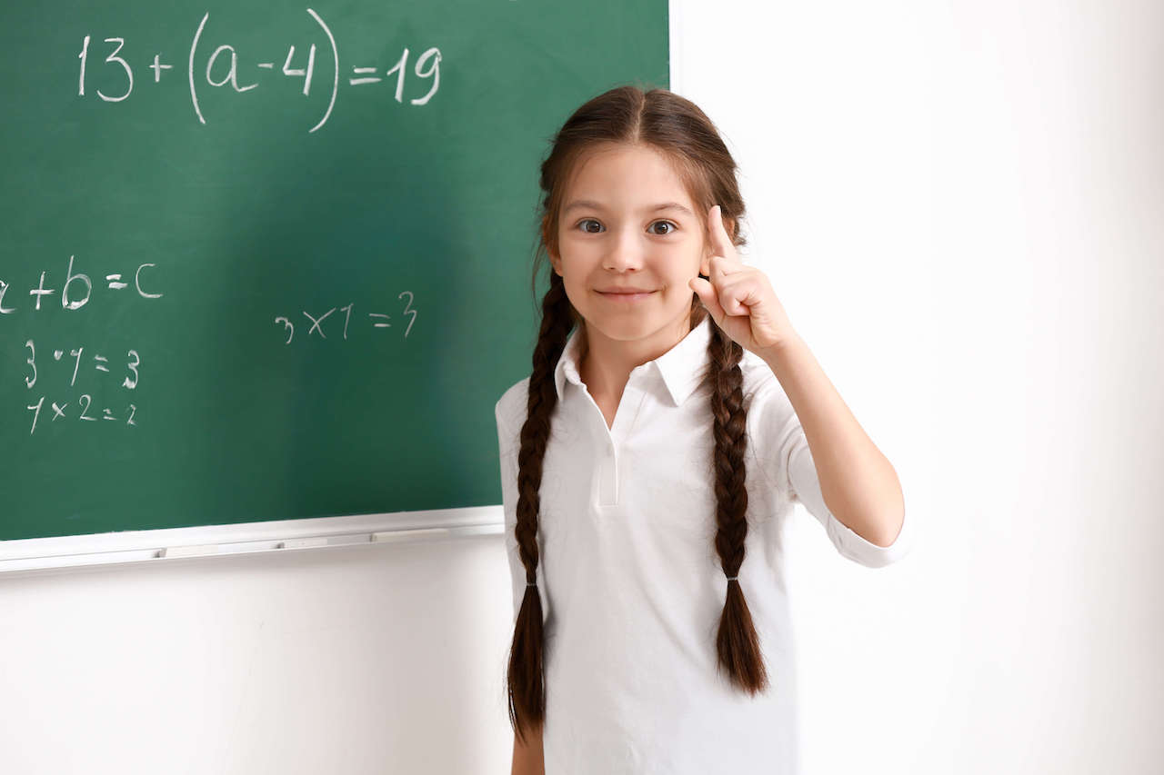 A child standing in front of a blackboard with algebraic variables written on it