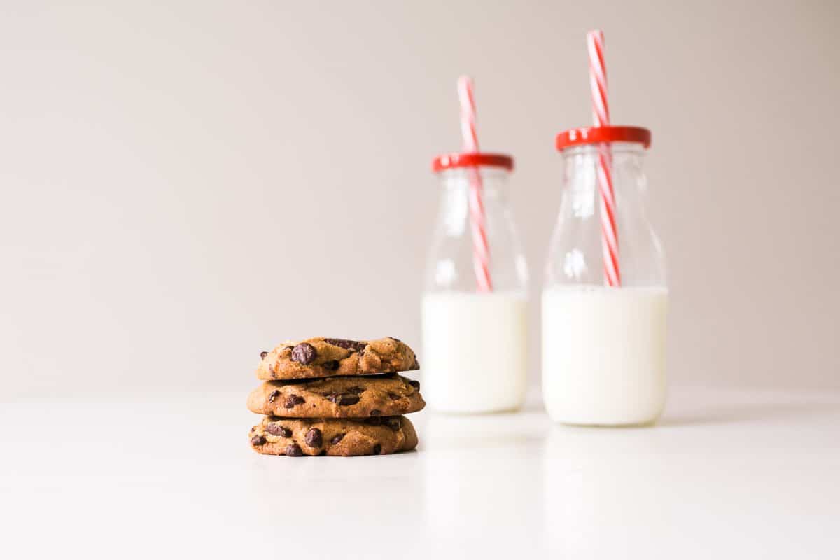 Three chocolate chip cookies and two jars of milk with red and white straws.