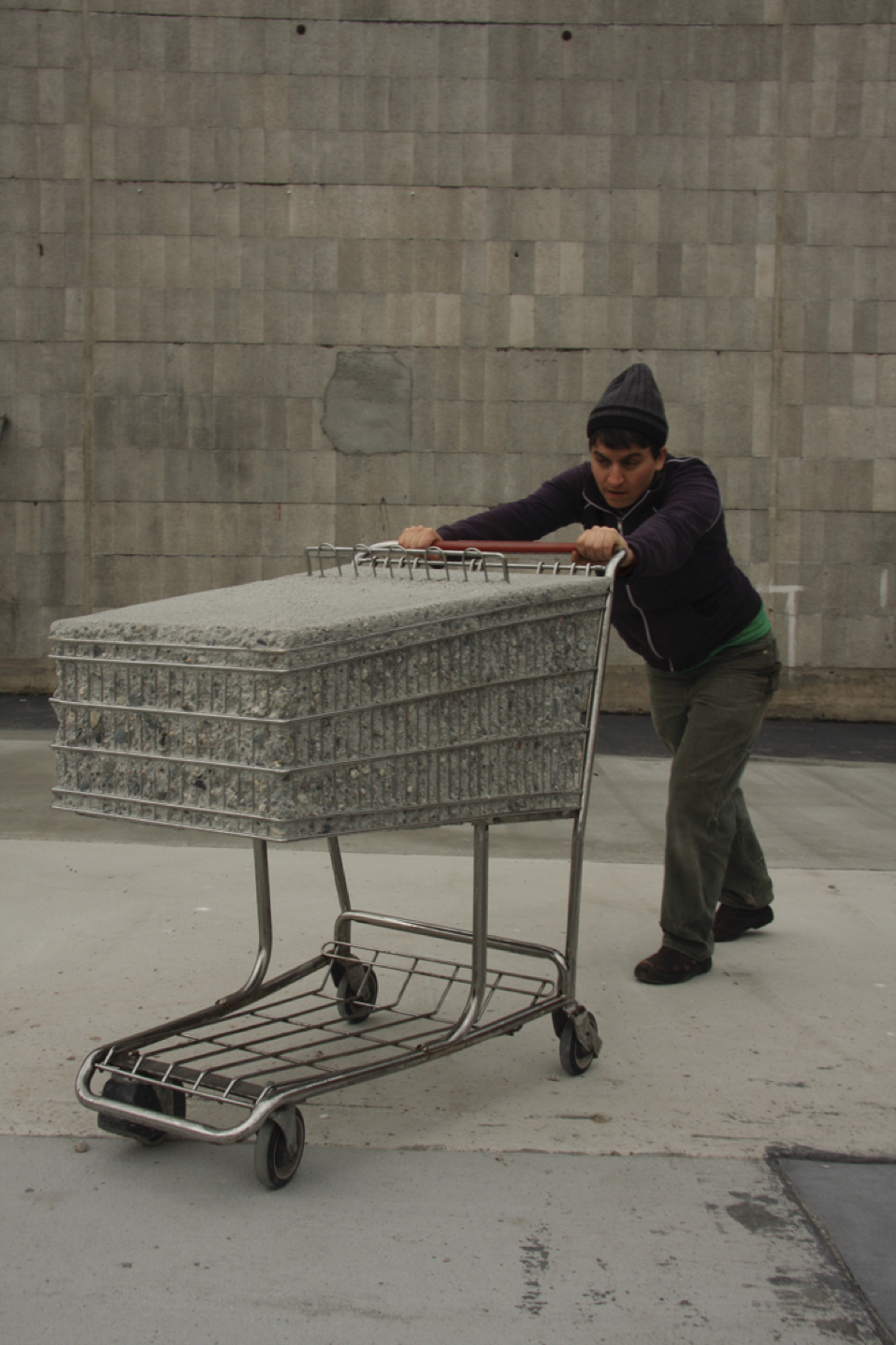 A man poses with "Smart and Final," a sculpture of a shopping cart filled with concrete, by pretending to push the cart. The sculpture is a manifestation of the weight of consumerism. (Photo courtesy of Terry Berlier)