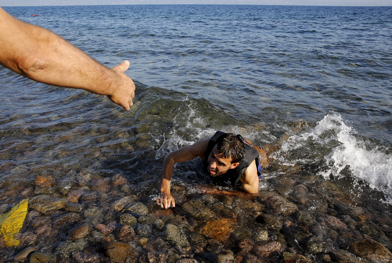 Local man helps a refugee who is swimming ashore.
