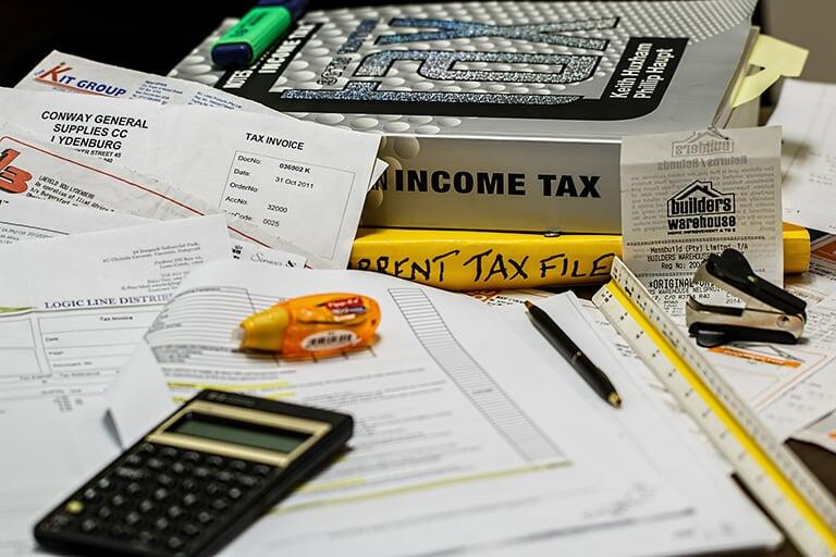 A desk of paperwork with a calculator and a income tax textbook next to it.