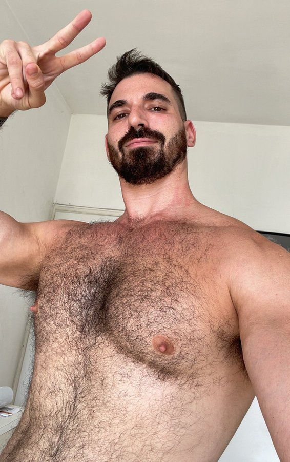 Thick Macho smiling and giving a peace sign for an smartphone selfie at home