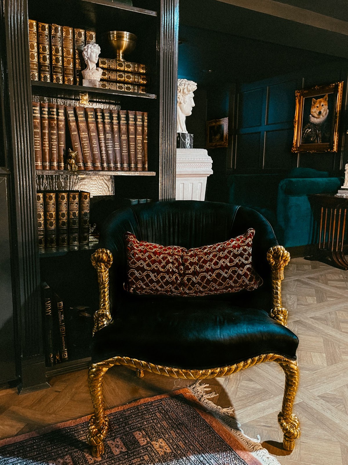 A reading corner anchored by a magnificent dark emerald green color on the wall and the furniture and complemented by the presence of a bookshelf filled with leather-bound books and charming busts.