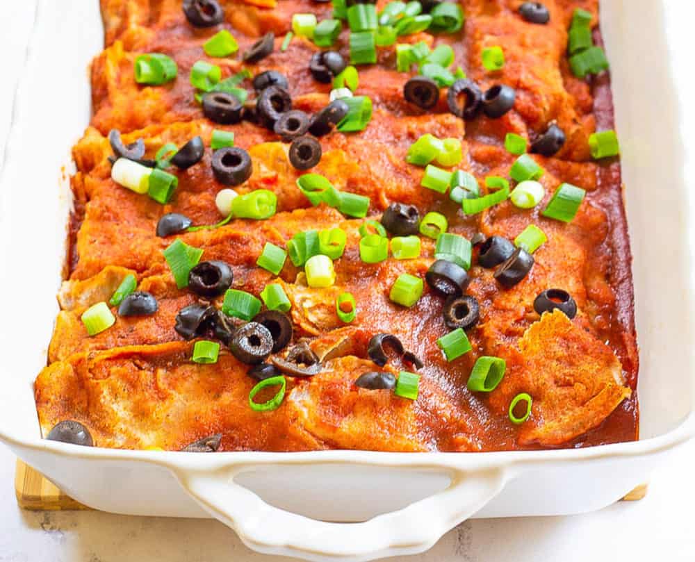 Vegan enchiladas served in a casserole dish and topped with green onions and olives.