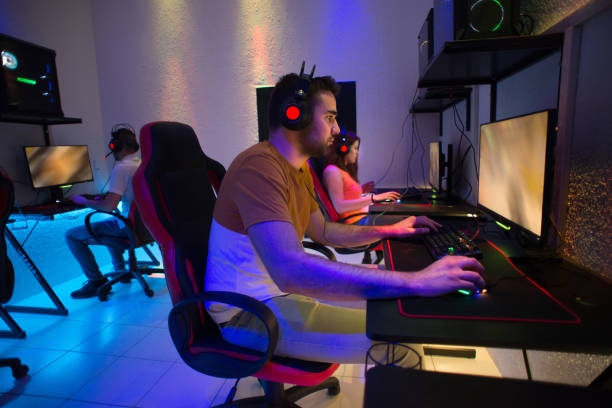 Gamers playing computer games Young gamers wearing gaming headphones with backlight and playing computer video games in dark gamers club. gaming chair stock pictures, royalty-free photos & images
