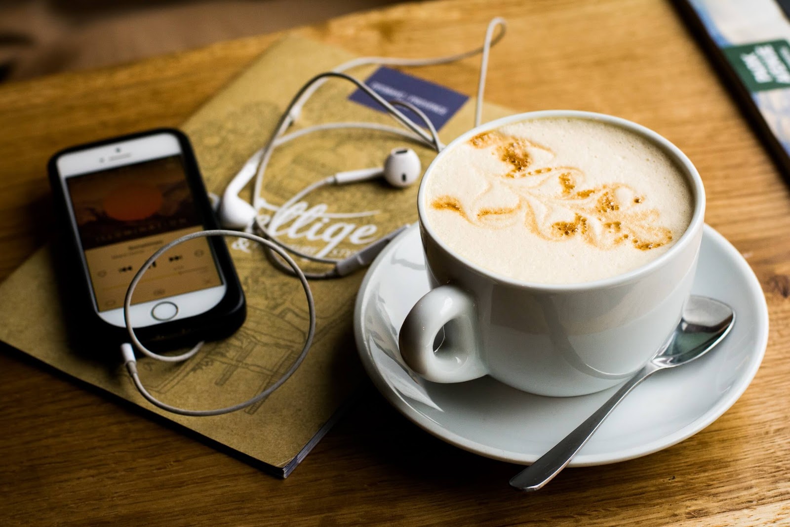 A phone with headphones, playing music on a coffee shop table