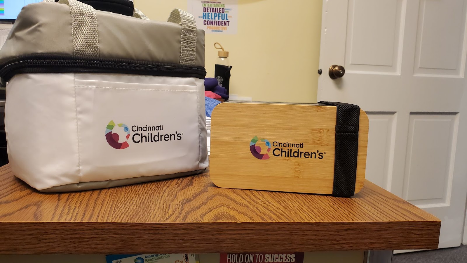 White and grey zippered cooler with fabric handles and wheat straw lunch box. Both items have the Cincinnati Children's Hospital Medical Center logo. 