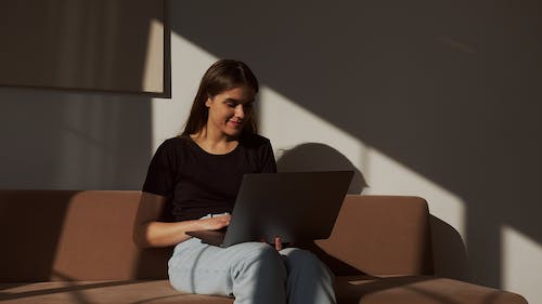 Free Positive woman surfing internet on laptop on sofa Stock Photo