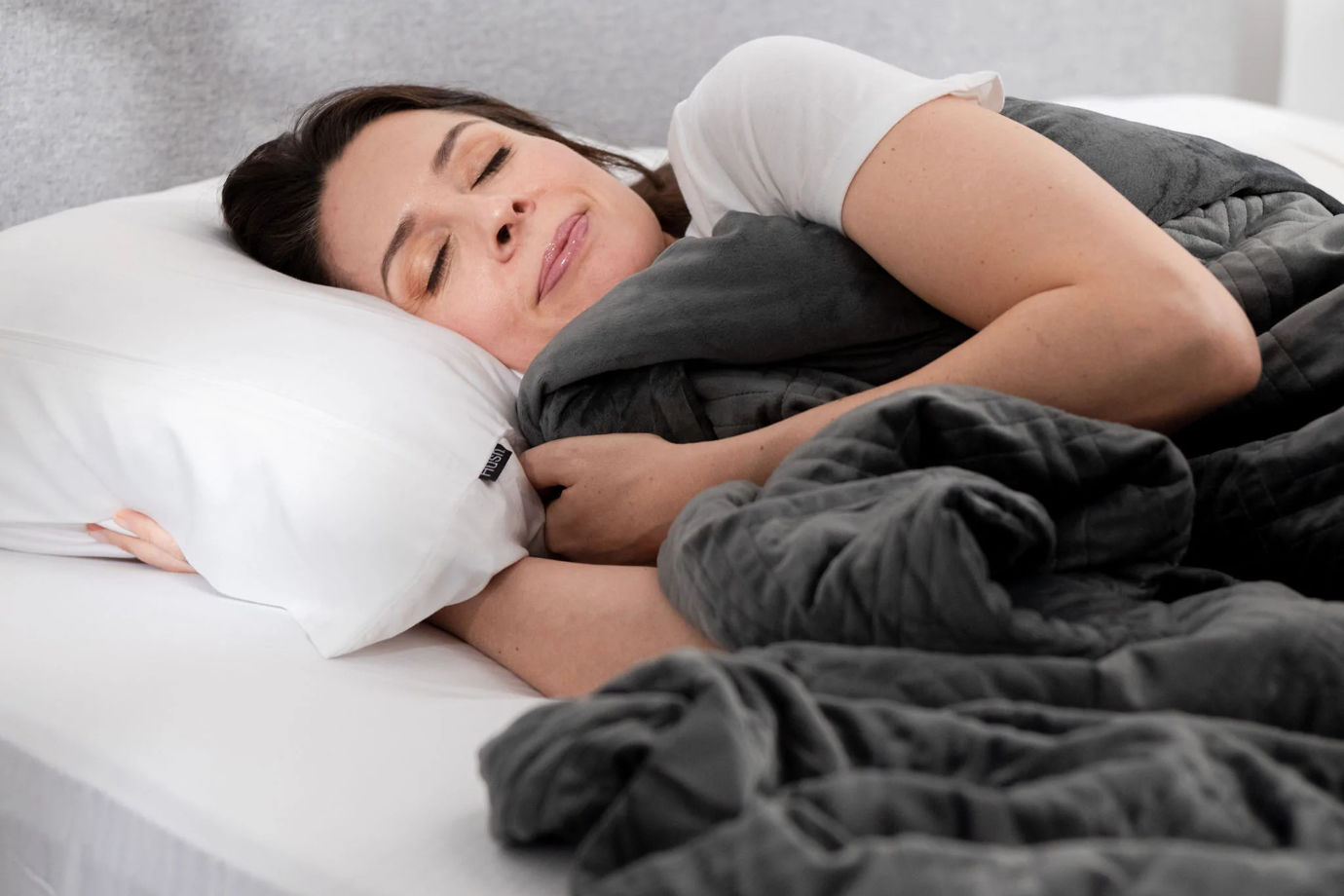 A woman sleeping comfortably in bed under a gray Hush Classic Weighted Blanket.