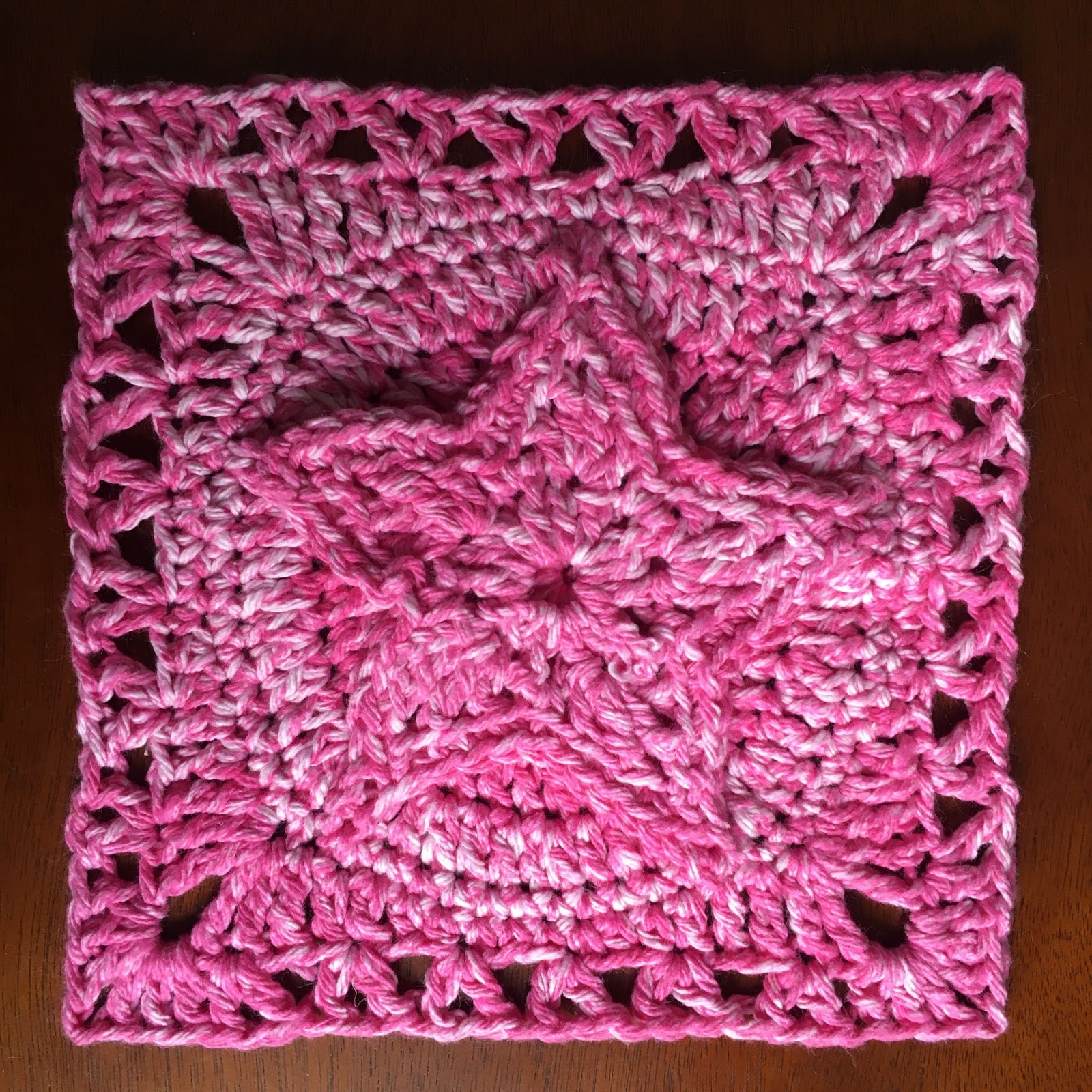 A pink crocheted square, with a raised star pattern on the top.