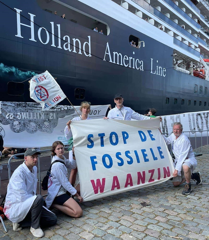 Rebel scientists hold a banner in front of a vast moored cruise ship