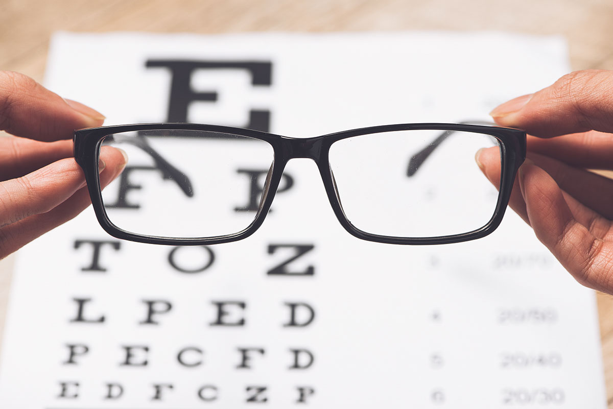 image of a pair of glasses being held in front of an eye exam letter sheet