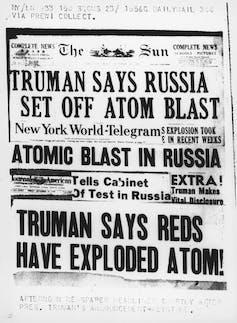 A black and white photograph shows newspaper headlines about Russia's atomic weapon testing.