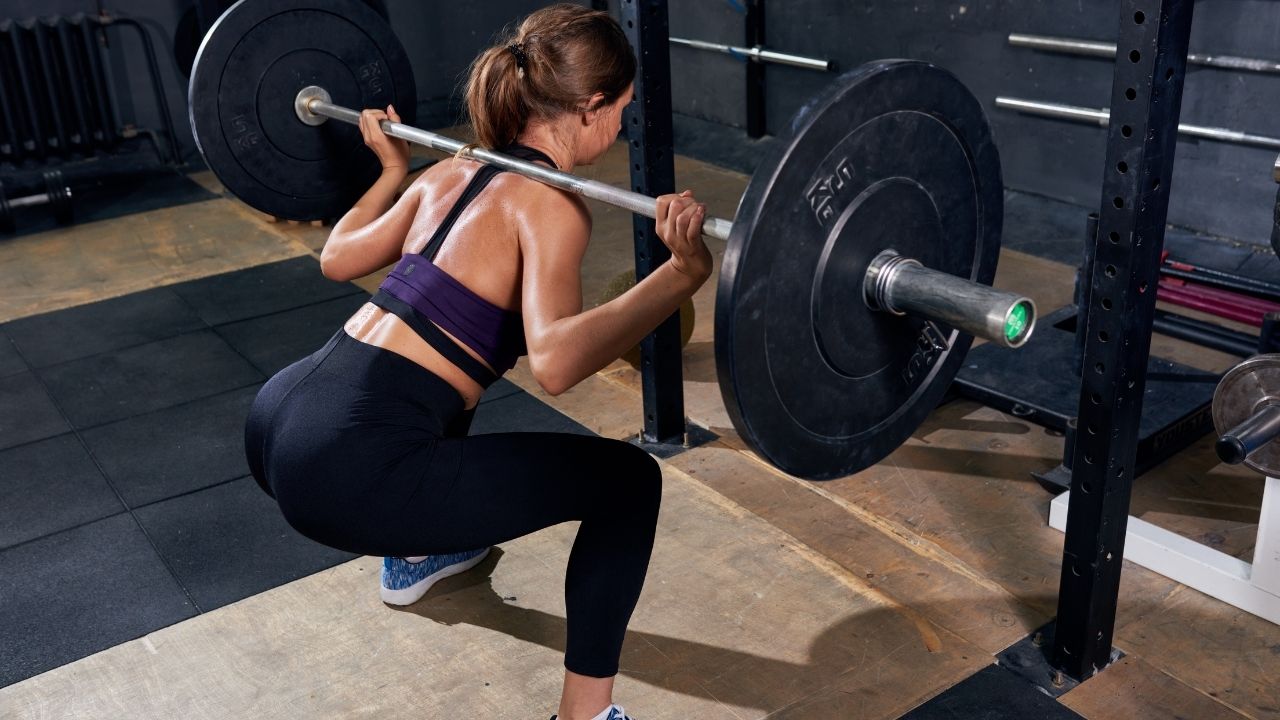 A woman performs barbell back squats in the gym.