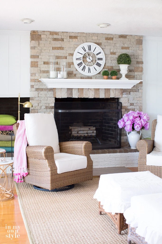 A room with white walls, wooden floorboards, and a stone fireplace area