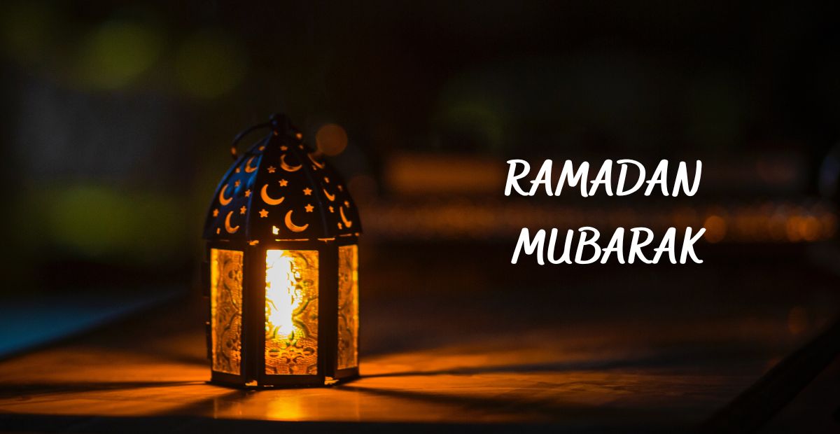 A Ramadan lamp with moon and star designs glowing in a dark background with a text "Ramadan Mubarak" in display