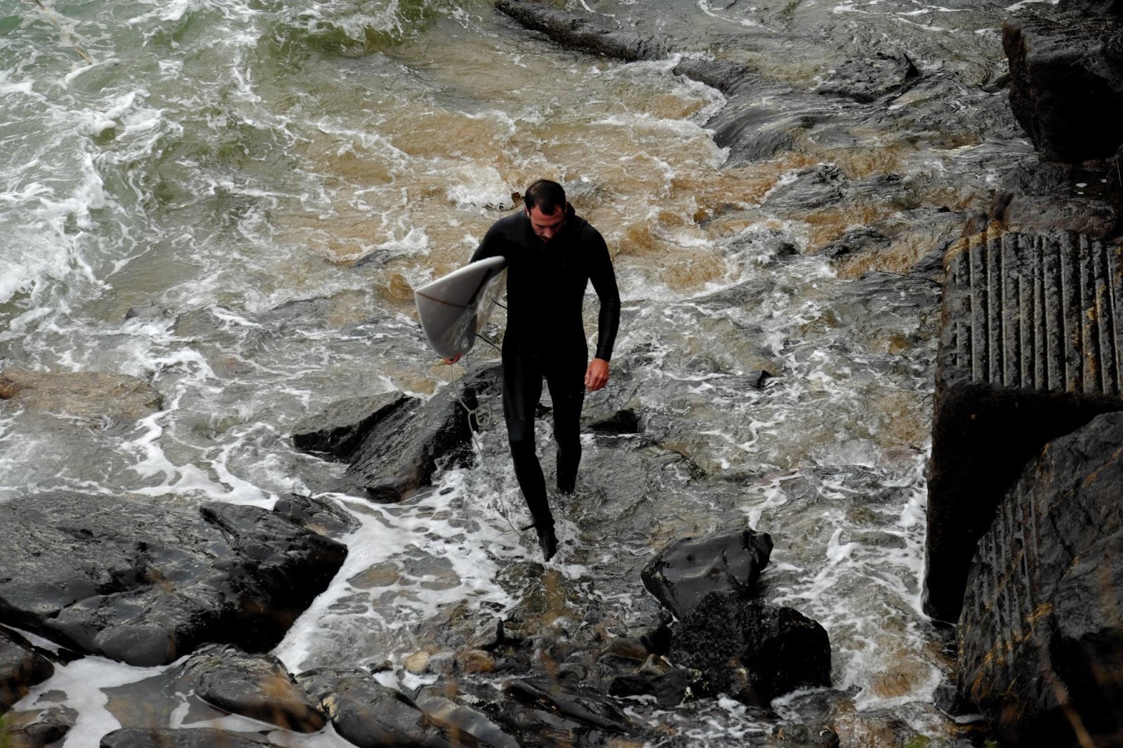 Muž jde se surfem a v neoprenu z vody.