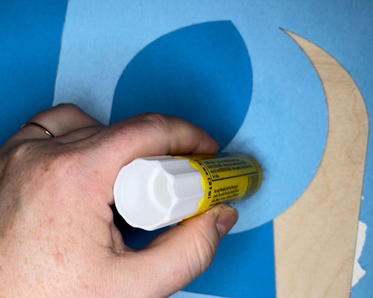 Hand applying glue to a blue piece of construction paper. 