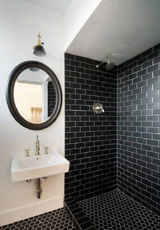 Banheiro com área do box revestida de azulejo subway tiles preto, piso ladrilhos hidráulico preto e uma parede branca com espelho de moldura preta.