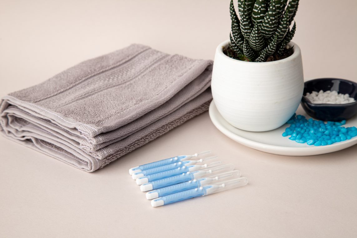 Imagem publicitária de alguns tipos de escova interdentais da marca Bitufo. Na imagem, também há uma toalha dobrada e um vaso de planta.