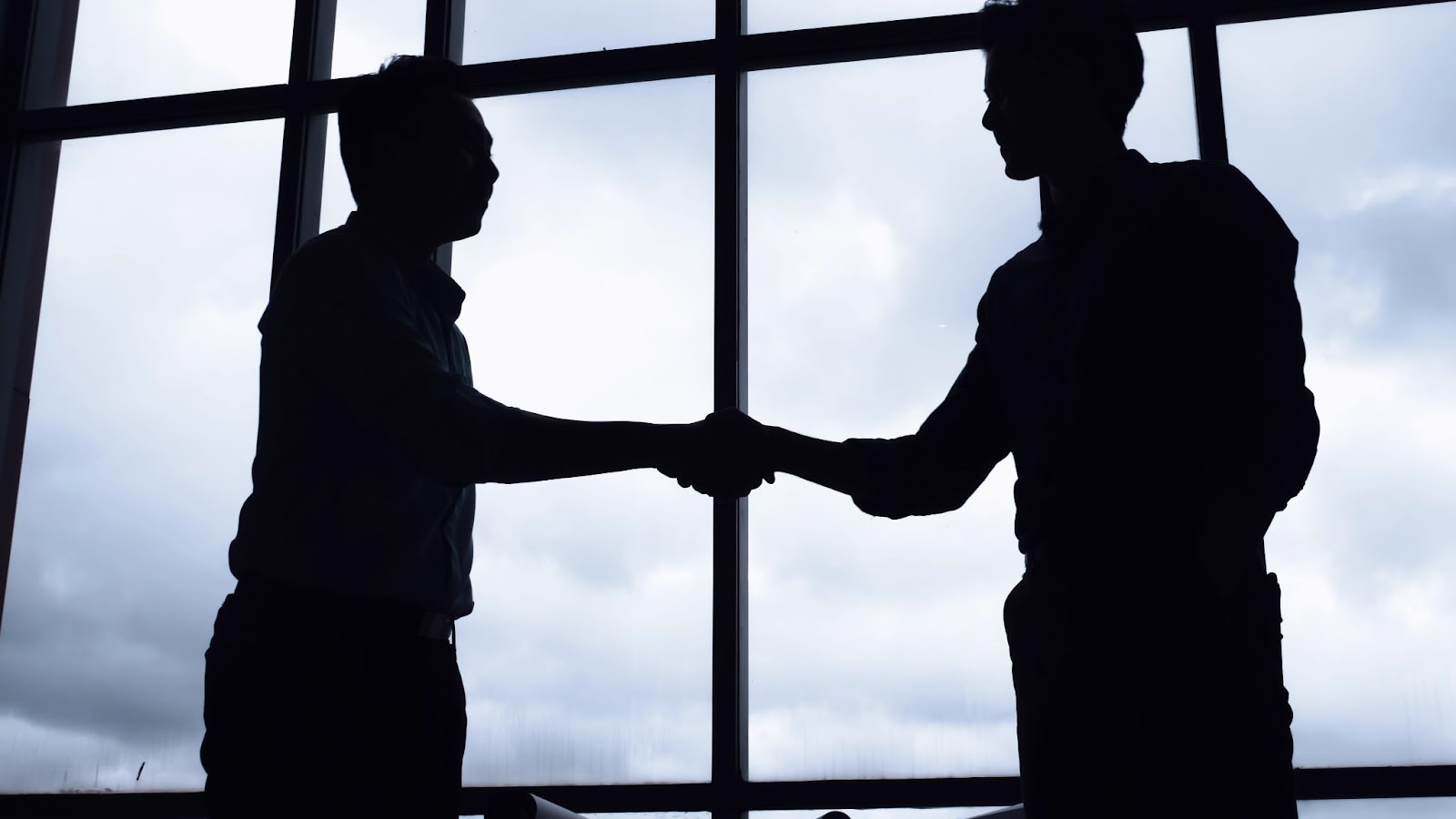 A show of two men in front of a high-rise window shaking hands