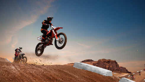 A pair of two dirt bike riders jumping off an exciting dirt hill, showing off their athletic ability. 