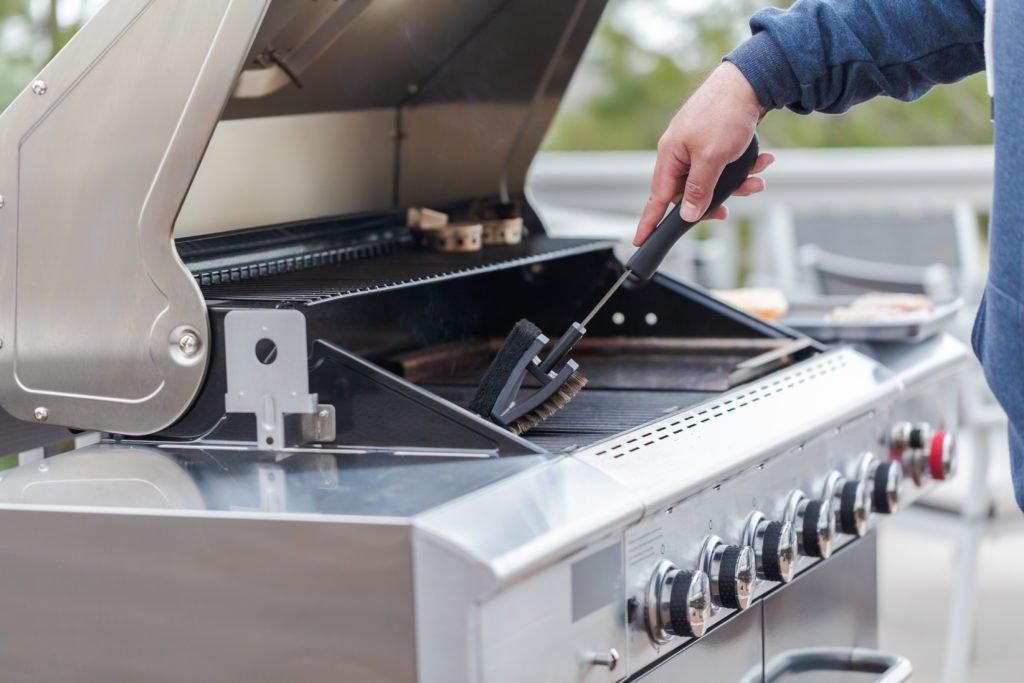 man cleaning the bbq with a brush with an open lid | WeServe