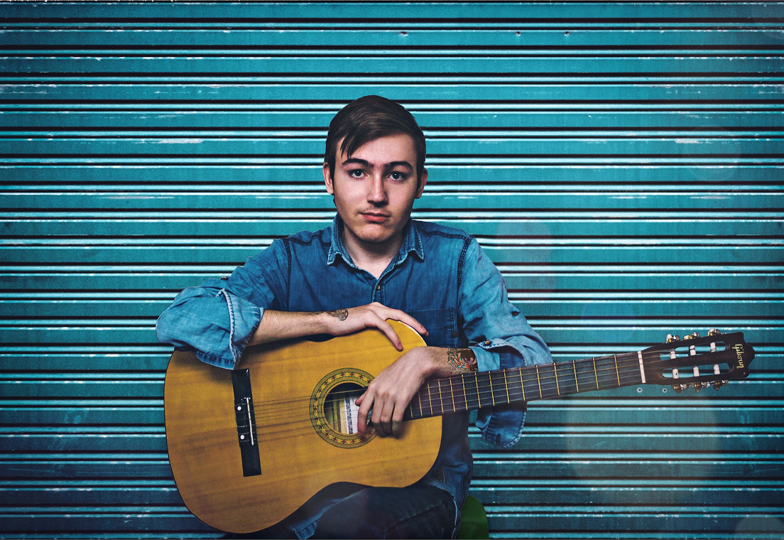 young man hold guitar against blue wall
