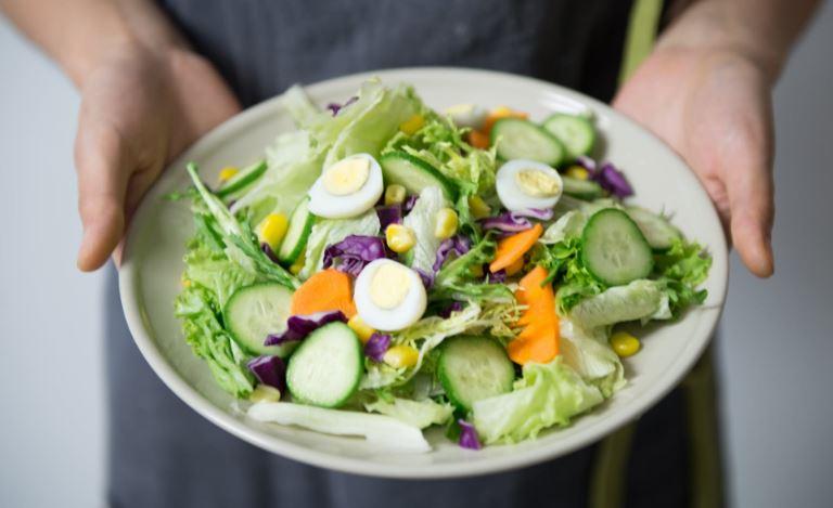 A person holding a bowl of salad

Description automatically generated